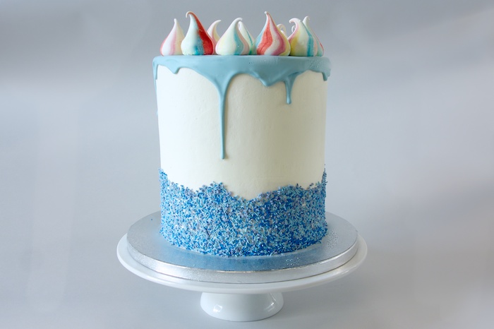meringues in white, with red and blue stripes, topping a tall white cake, with blue frosting, and sparkly blue decoration