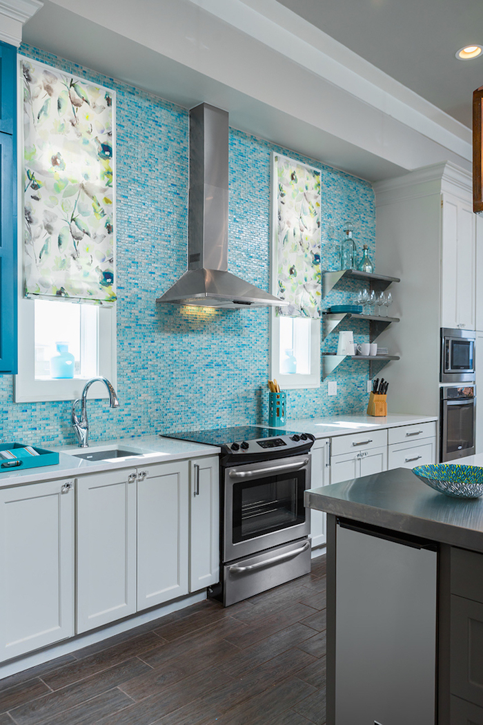 window blinds in white, with floral motifs, in a kitchen with white cabinets, teal blue and white glass mosaic tile backsplash, and dark wooden floor