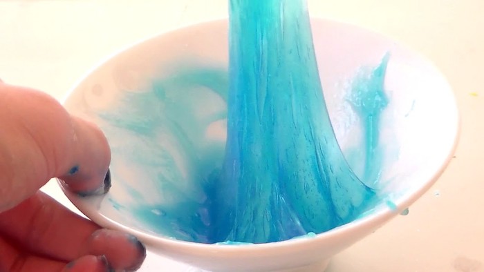 sticky slime in light teal, pulled from a white ceramic bowl, held by a person's hand, stretchy gum-like substance