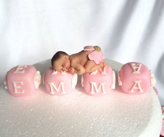 emma spelled out by pink alphabet cubes, with white letters, made from fondant, and decorated with a realistic sleeping baby figurine, in a pink flower nappie, baby shower cake toppers girl