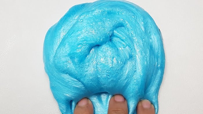 fingers pressing on the edge, of a turquoise pile of goo, shiny and slimy, how to make slime with borax, placed on a white surface