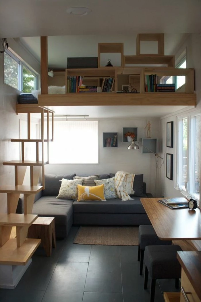 compact space with black tiled floor, and a second story with bookshelves, simple living room designs, grey corner sofa, with several cushions