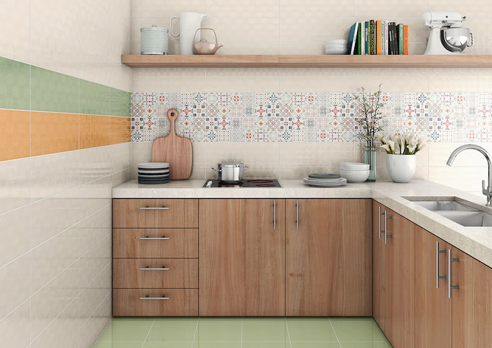 various kitchen utensils, off-white counter tops, and pale brown cabinets, in a room with an arabesque backsplash, and tiled walls