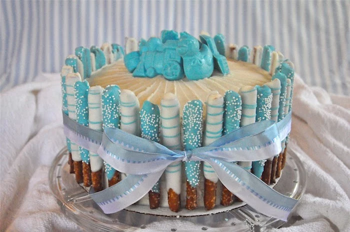 train and duckling, and other shapes, made from pale blue fondant, and placed on a creamy cake, lined with pretzel sticks, dipped in light blue and white frosting