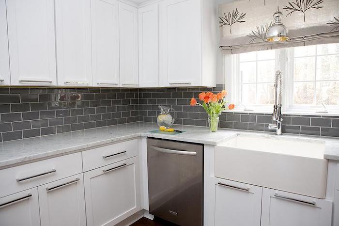 grey subway tile pattern, on the wall of a kitchen, with smooth and white, modern sink and matching cabinets, clear vase with tulips