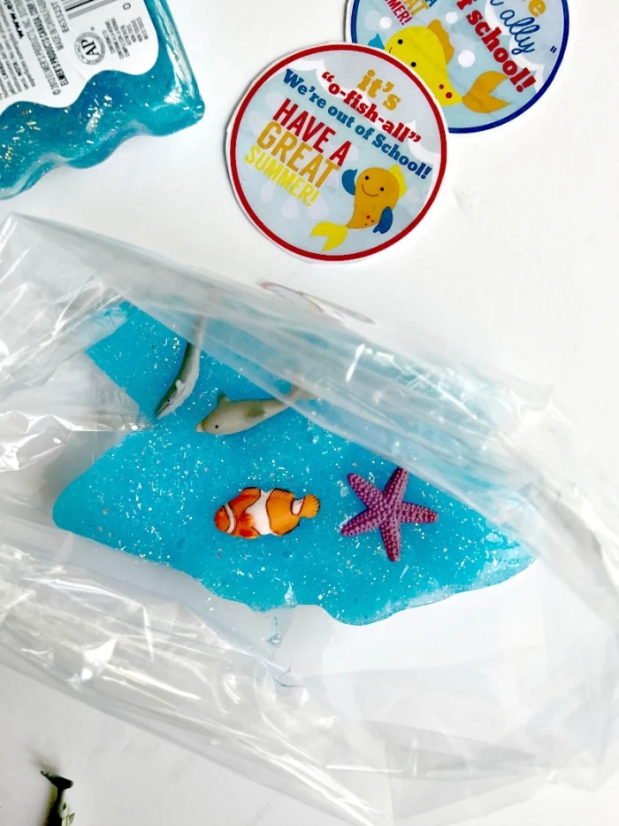 fish made form plastic, and some glitter, decorating a turquoise piece of goo, how to make slime with shaving cream, placed inside a clear plastic bag