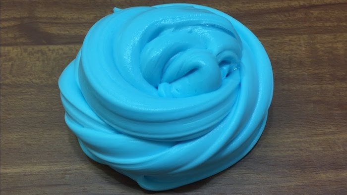 twisted pile of turquoise goop, shiny and slimy, how to make fluffy slime, twisted and placed on a dark wooden surface