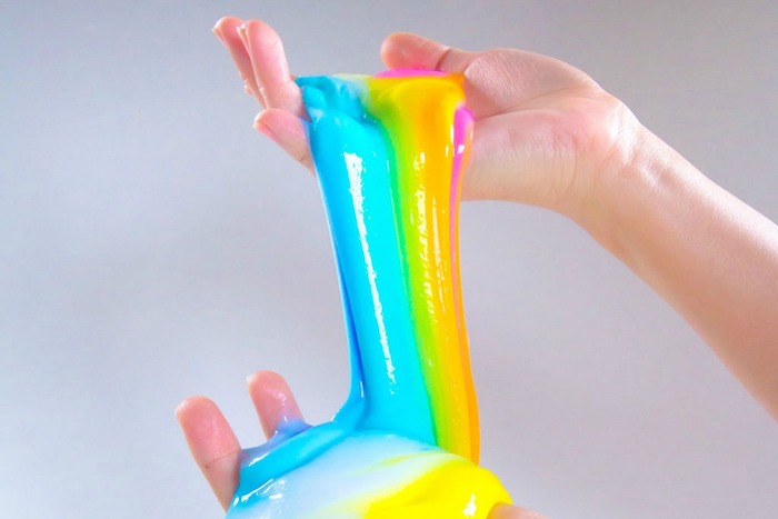how to make slime without borax, two hands holding a stretchy, slimy and smooth goo, striped in different colors, blue and green, yellow and pink