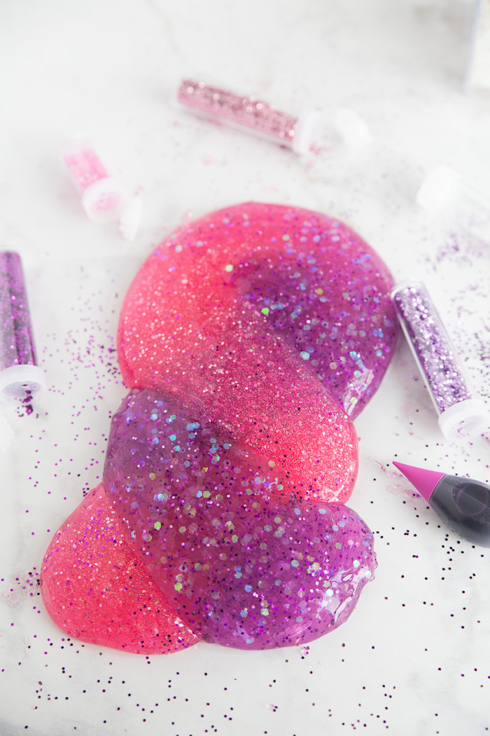 several vials of glitter, in pink and purple, near a piece of purple and pink, elmer's glue slime, twisted into a braid-like shape