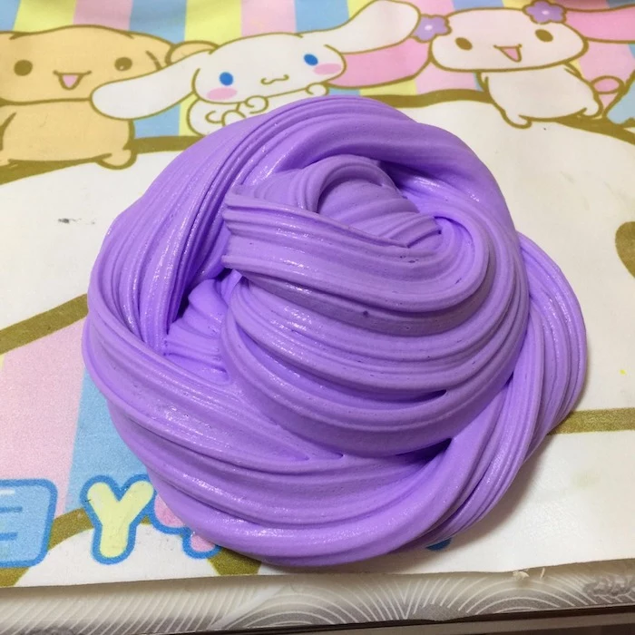 purple piece of goop, twisted into a roundish shape, how to make fluffy slime, placed on a colorful surface, with pastel colors, and cartoon drawings