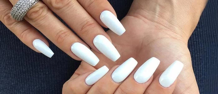 pure white nail polish, on two hands with four visible nails, one hand has a chunky, encrusted silver ring on its ring finger, coffin nails