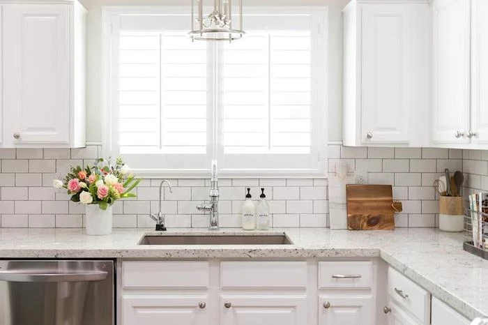 bouquet in a white vase, placed on a marble counter top, near two windows, white subway tile pattern, and matching white cabinets