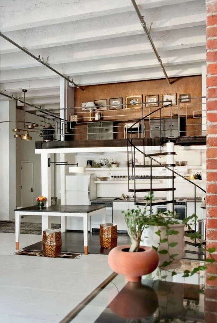 industrial style studio flat, with a winding wrought iron staircase, containing a large black and white table, home decor inspiration, a kitchenette and some shelves