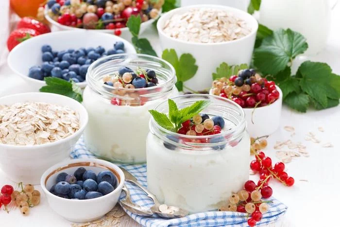 berries of different kinds, topping two small glass jars, filled with yoghurt, healthy low calorie breakfast, dishes with rolled oats, blueberries and other fruit