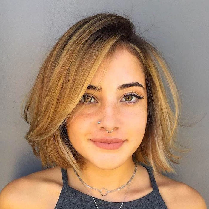 freckled young woman, with auburn hair, styled into a bob, with deep side part, and dark roots, easy short hairstyles, wearing a dark grey tank top, and nose piercings