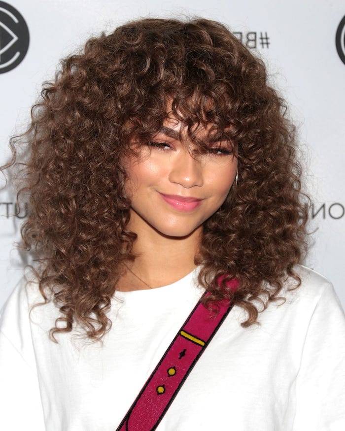 t-shirt in white, with pink and yellow print, worn by zendaya, chocolate browncurly hair with bangs, small natural ringlet curls