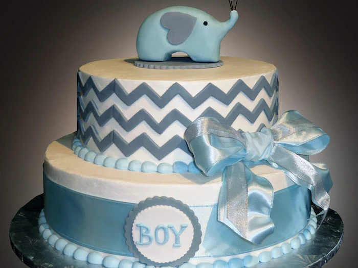 elephant baby shower cake, white with two layers, decorated with shiny blue ribbons, and blue zig-zag shapes, the word boy, written with blue frosting