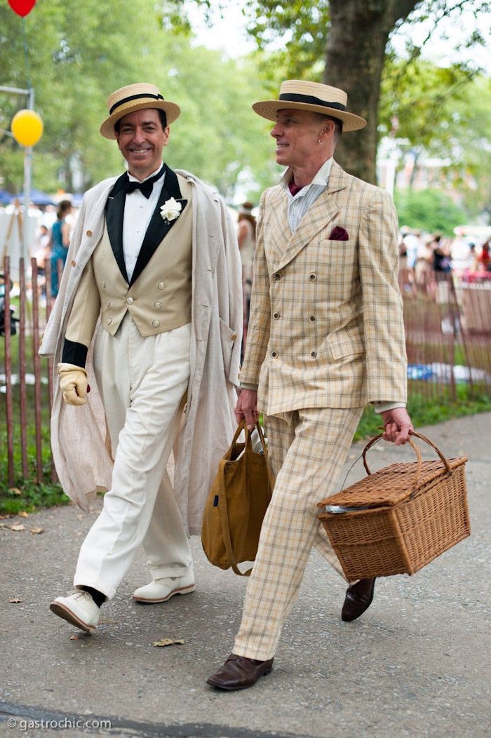 roaring 20s fashion, two smiling men, wearing cream and white 1920s suits, and falttop hats, walking on a street, one of them is holding a picnic basket, great gatsby themed party outfit