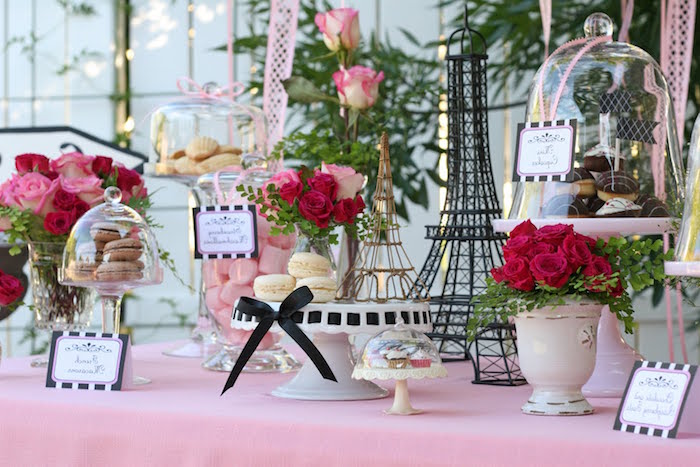 eiffel tower decorations, and several bouquets of red and pink roses, on a table with a pale pink tablecloth, containing macarons and various other kinds of sweets, French themed party, 60th birthday ideas