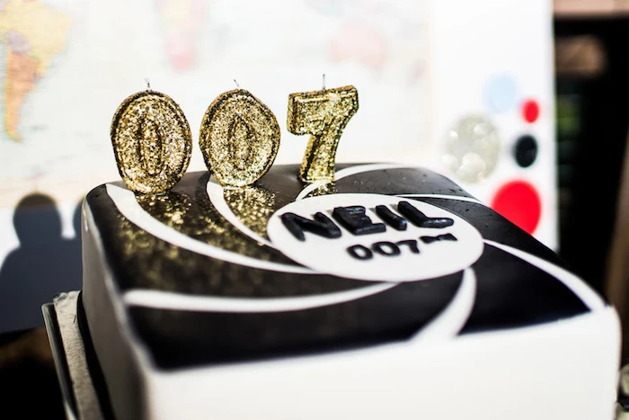 3 candles shaped like the numbers 007, in a sparkly gold color, on a black and white cake, 60th birthday party ideas, James Bond inspired decoration