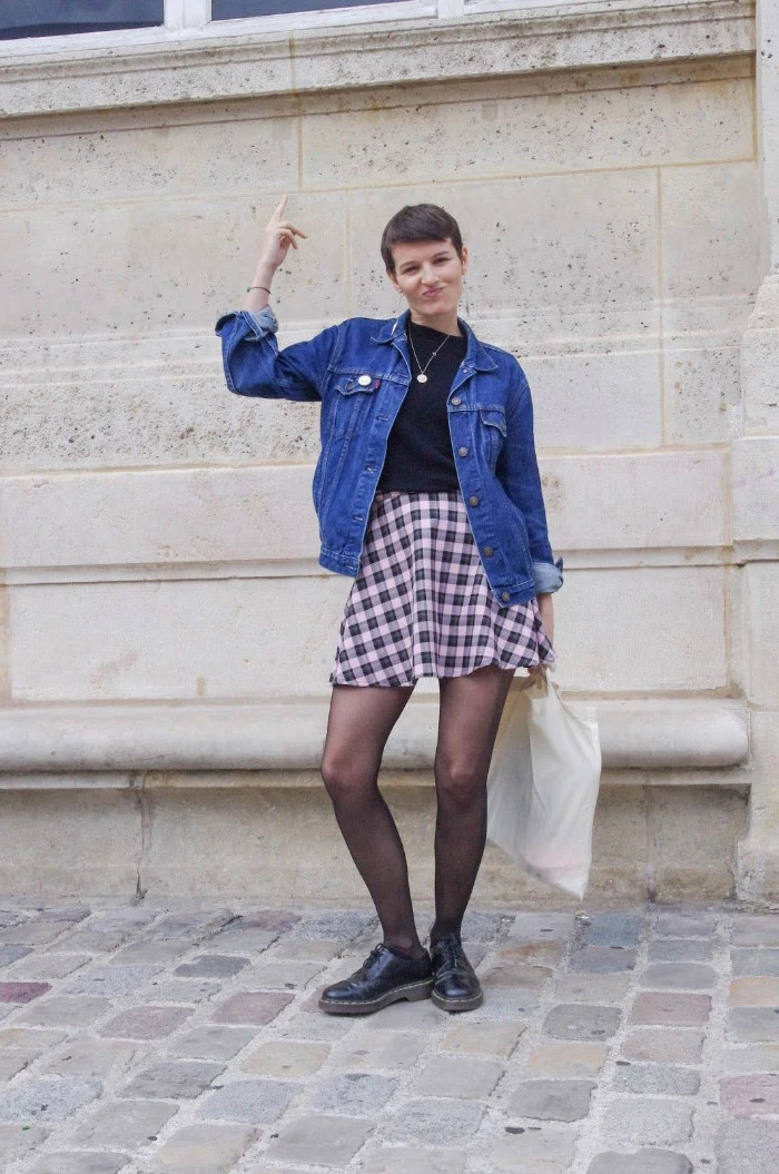 pixie cut worn by young brunette woman, in a pale pink and black plaid skirt, 90s inspired outfits, black top and an inky blue denim jacket