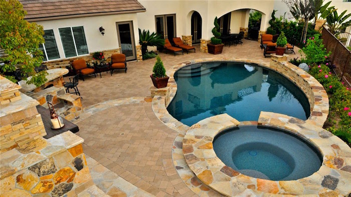 small inground pools, a set of two, surrounded by beige, and pale brown stone tiles, in a garden near a house