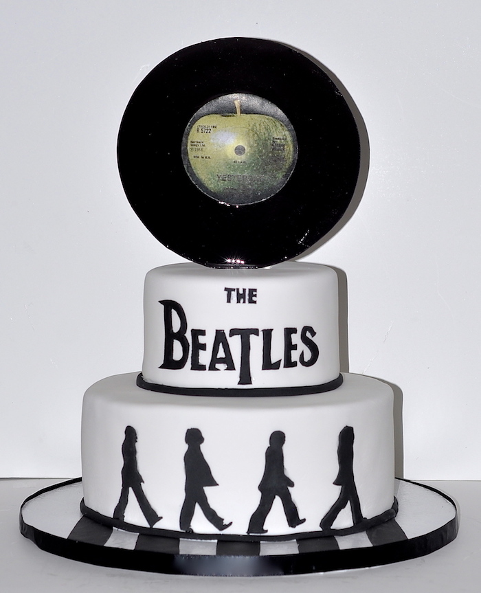 the beatles crossing abbey road, painted in black on a white cake, topped with a vinyl record, with the drawing of a green apple