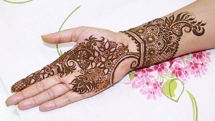 fabric in white, with pink and green print, under an arm, henna hand tattoo designs, on its palm and wrist