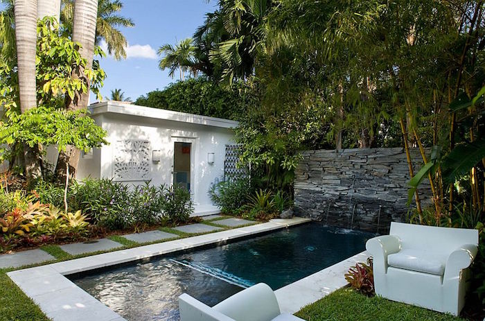 palm trees and various shrubs, in a garden with a small white shed, and a rectangular swimming pool, cool backyards, two white armchairs