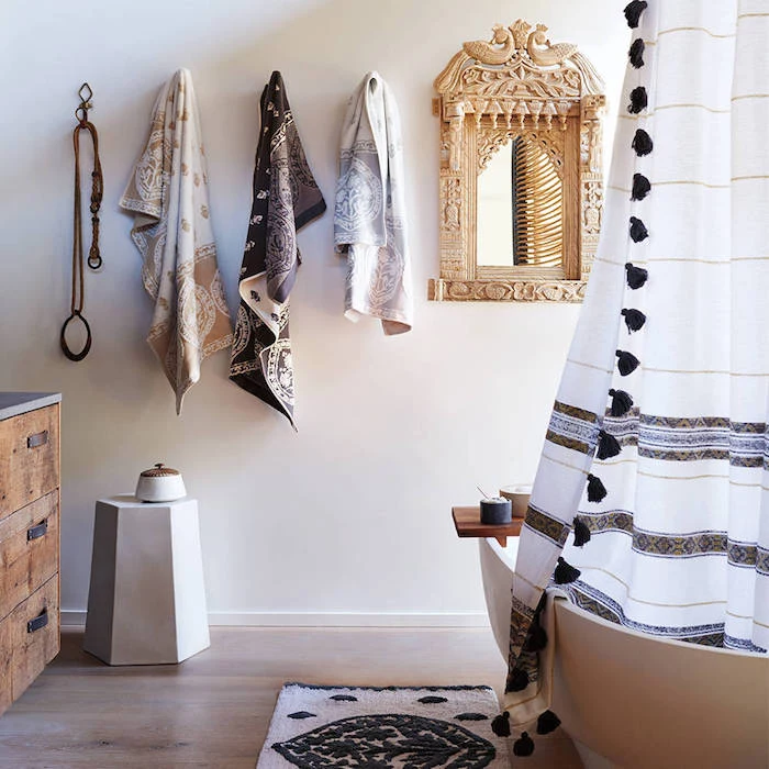 three towels with beige, brown and grey patterns, hanging on a white wall, near a mirror in an ornate frame, and a white bathtub, diy bathroom decoration