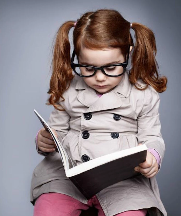 classic pigtails with a deep side part, simple hairstyles, on the auburn hair, of a small girl, with large glasses, holding an open book
