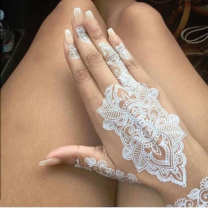 french fade nails, on a hand with a large, white mock-henna temporary tattoo, resting above a woman's bare legs