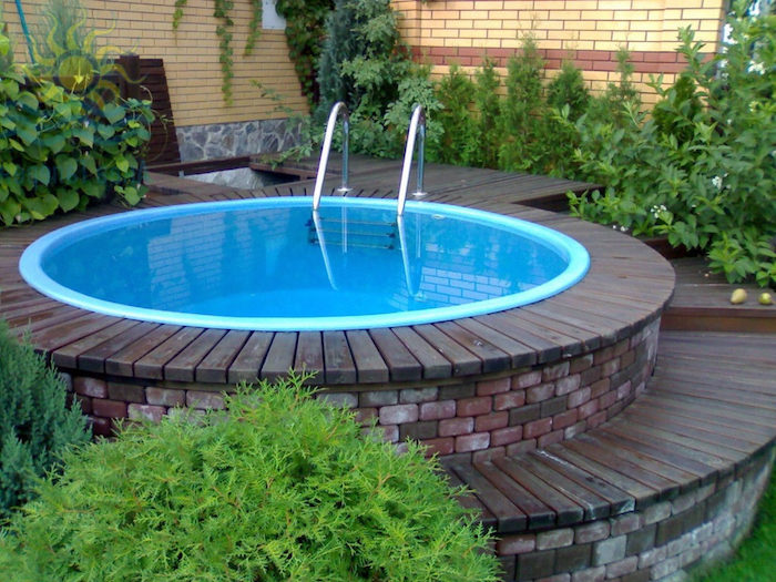 green shrubs and flowers, near a small, circular elevated pool, lined with bricks, and wooden planks, cool backyards