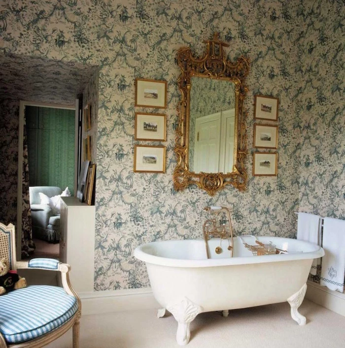 claw-footed antique bathtub in white, inside a room with a baroque-style, floral wallpaper in cream and green, mirror in ornate gold frame