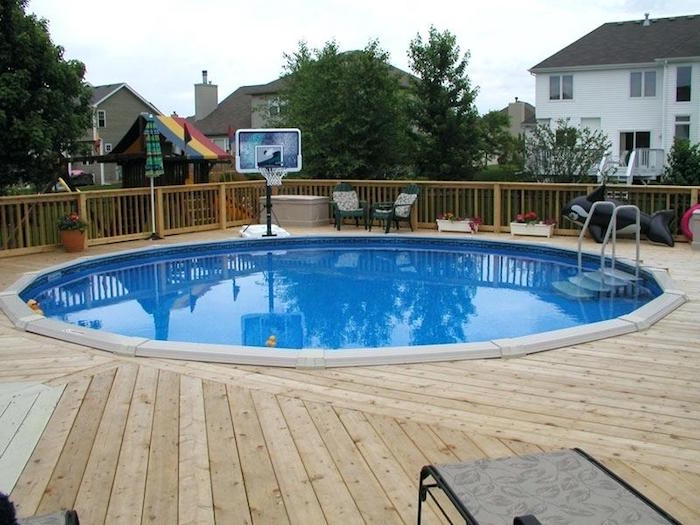 inflatable toy and a basketball net, near a circular pool, in a yard, covered by wooden planks, pool patio ideas, neighborhood houses in the background