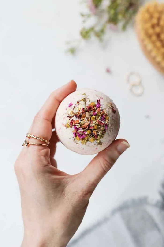 bath bomb with dried flowers inside, held by a female hand, wearing gold rings, creative diy christmas gifts