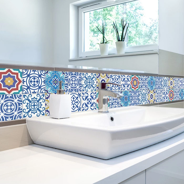 patchwork of multi-coloured Moroccan tiles, near a large wall mirror, and a modern white stink, with a silver metal faucet, bathroom wall decor ideas, two potted plants in a window
