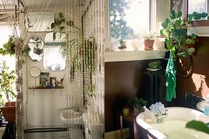 small bathroom décor, two examples of boho bathrooms, one with several mirrors on the wall, a beaded curtain, and lots of potted plants, and one with brown walls, and a white bathtub