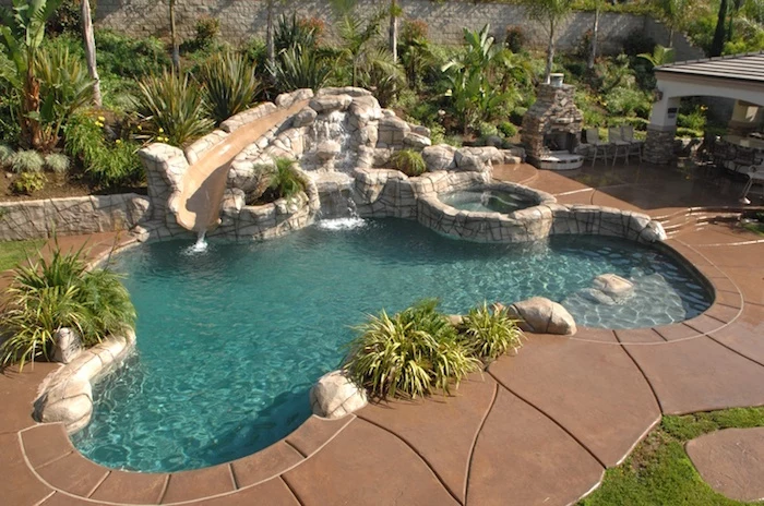 decorations made of stone, around a small pool, surrounded by beige stone tiles, cool backyards, spout-like construction, pouring water into the pool