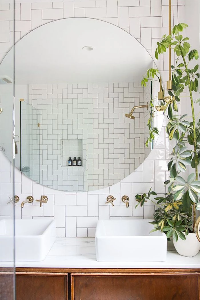 herringbone subway tiles in white, and a large round mirror, in a room with two sinks, and a potted plant, bathroom decorating ideas on a budget, retro wooden cupboard