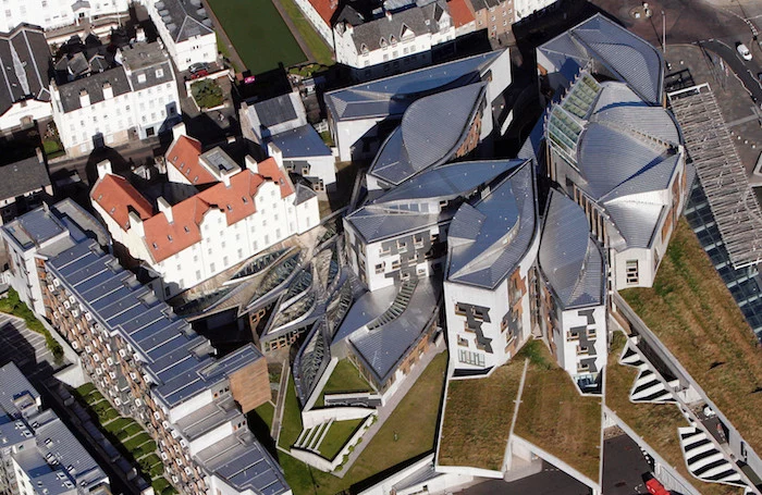 areal photo of the scottish parliament building, postmodern design, with several detached structures, each in an asymmetrical shape, with a grey roof