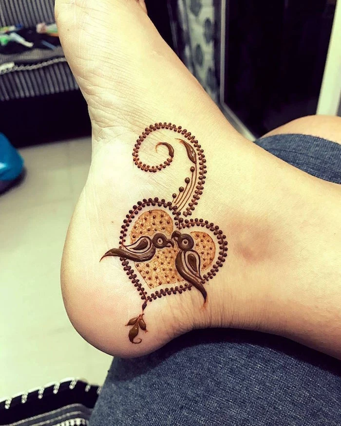 a heart with flourishes, and two little parrots, painted with brown henna, on the heel of a foot, henna foot tattoo
