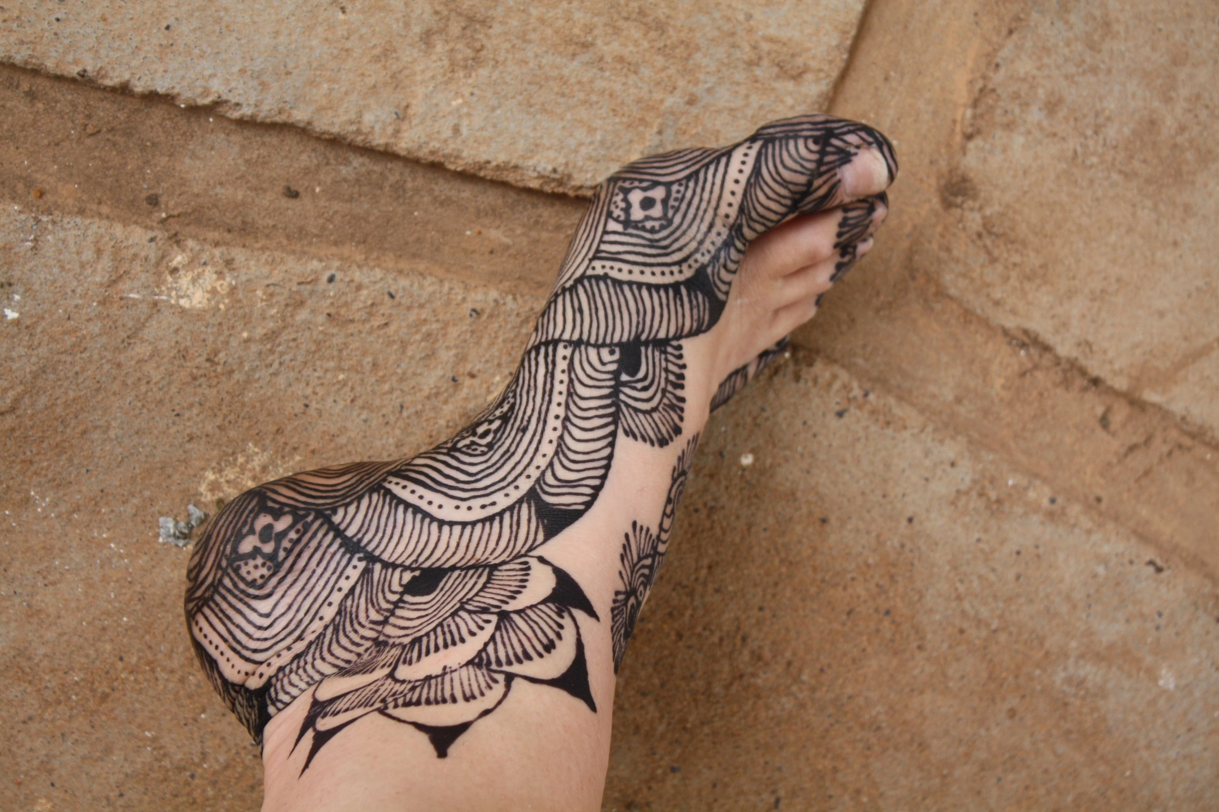 ornamental black henna tattoo, on the sole and ankle of a leg, resting on the ground, temporary henna tattoos