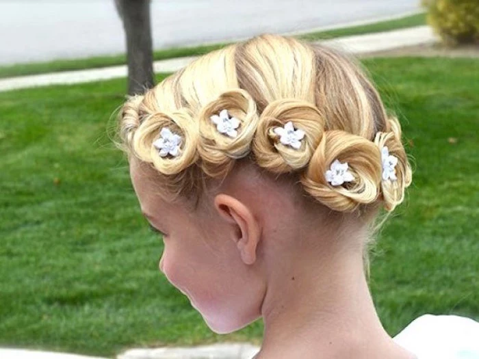 swirls of blonde hair, decorated with tiny, white blossom ornaments, on the head of a small child, flower girl hairdos