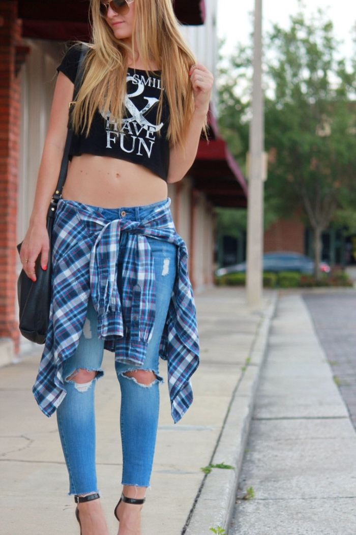 90s clothes womens, cropped black t-shirt, with white print, ripped jeans and a flannel shirt, tied around the waist