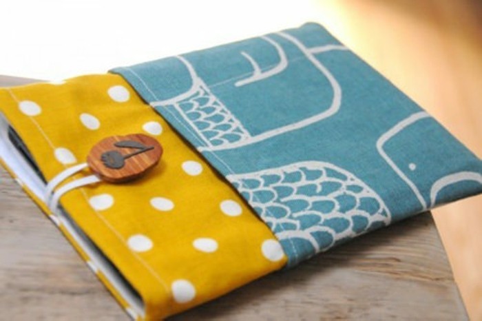 fabric book cover, in mustard yellow, and teal blue, decorated with white polka dots, and off-white patterns, and a wooden button, cute gift ideas
