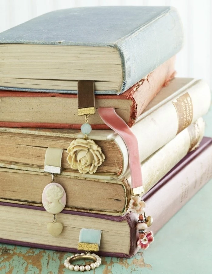 stack of vintage books, most containing diy bookmarks, made with suede straps, in different colors, and jewelry-like charms, last minute birthday gifts, cameo brooch and rose ornament
