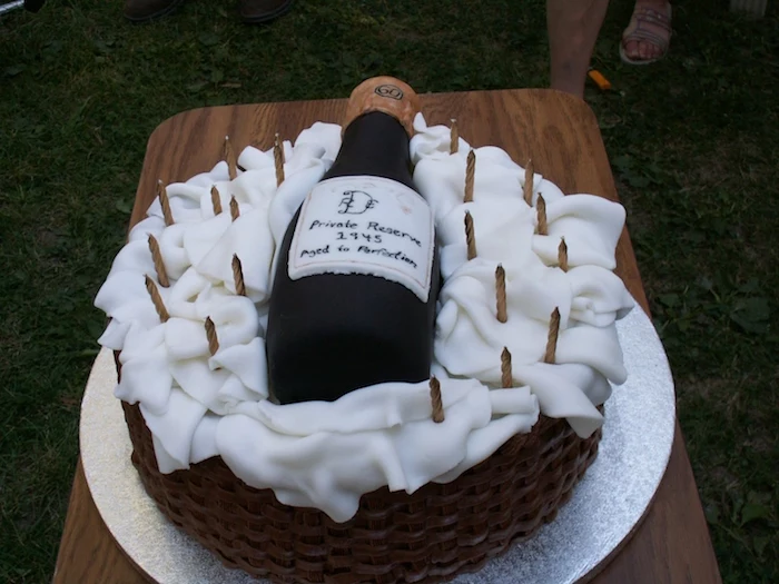wine bottle-shaped cake in black, with a white label, placed on a basket made from fondant, unusual birthday cake ideas