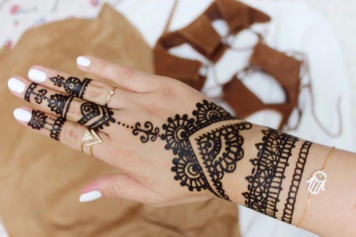 rings and a bracelet, made of gold, decorating a hand, painted with black, temporary henna tattoos, and sporting white nail polish