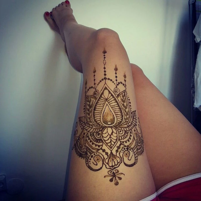 large temporary tattoo, covering the thigh of a woman, wearing red and white shorts, cute henna, lotus-like details and flourishes